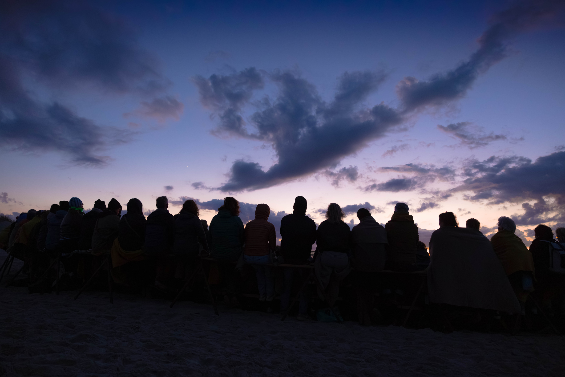 Groep festivalgangers als silhouet op het strand van Terschelling, kijkend naar een paars-blauwe avondhemel tijdens Oerol Festival.