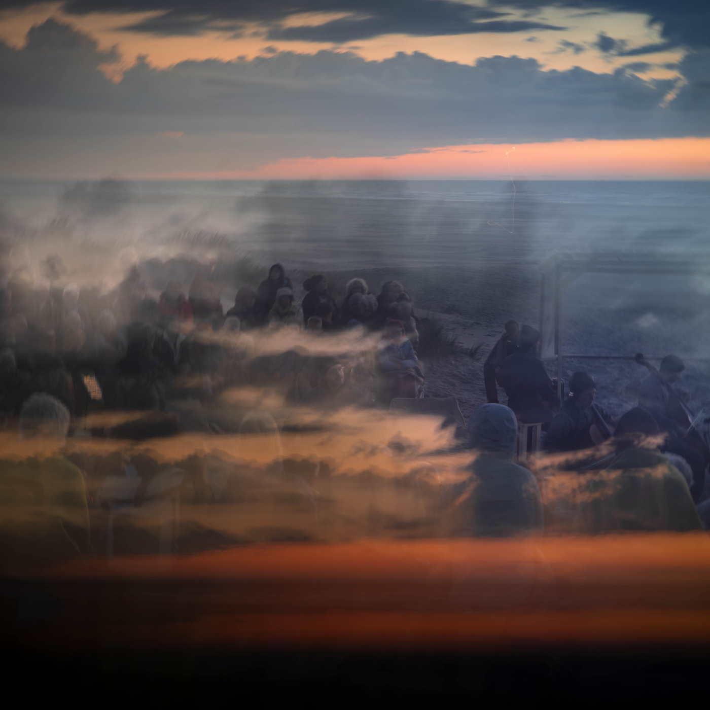 Meervoudige belichting van festivalgangers op Terschelling tegen een dramatische zonsondergang boven zee, tijdens Oerol Festival.