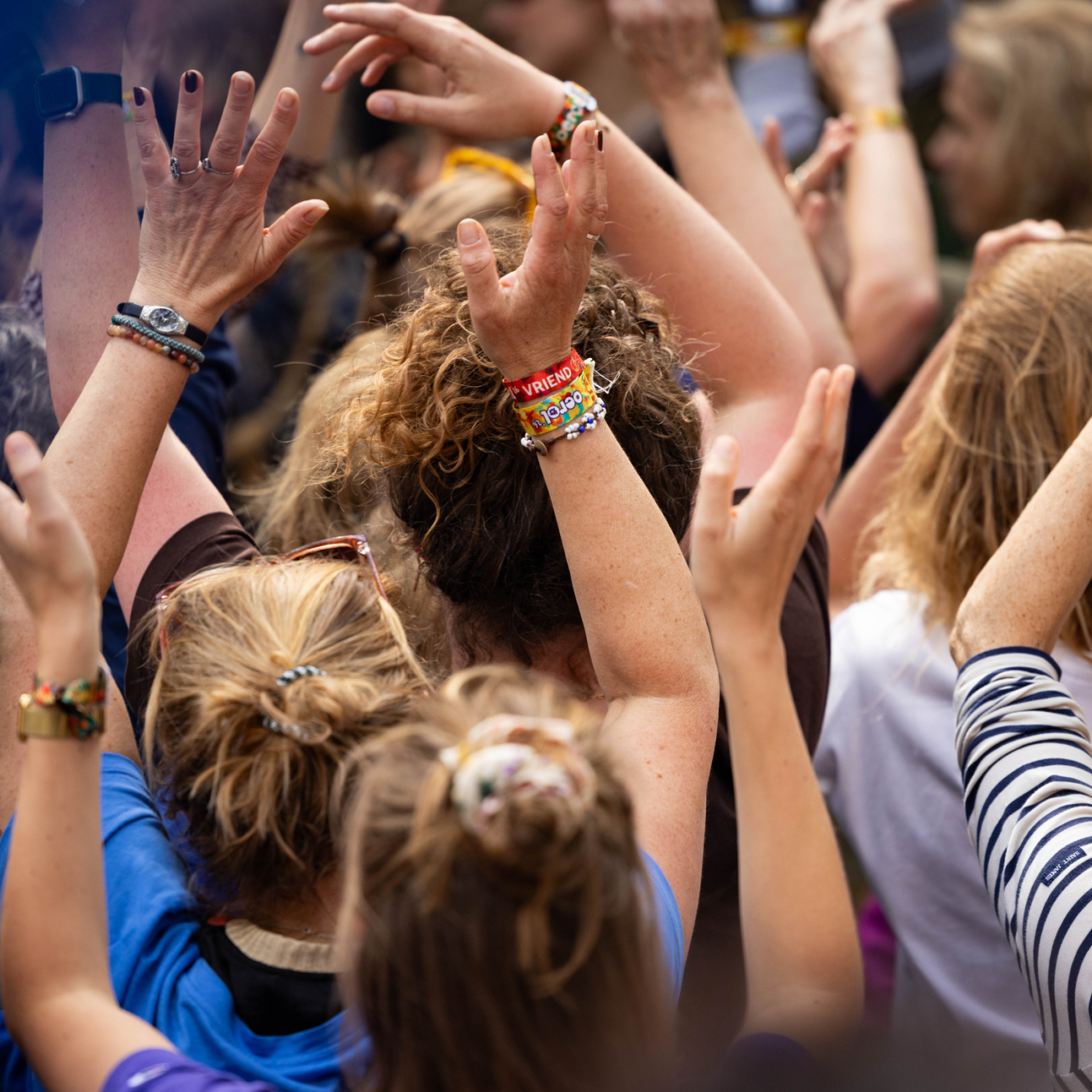 Enthousiast publiek steekt handen omhoog tijdens Oerol Festival op Terschelling, met kleurrijke festivalpolsbandjes zichtbaar aan de polsen.