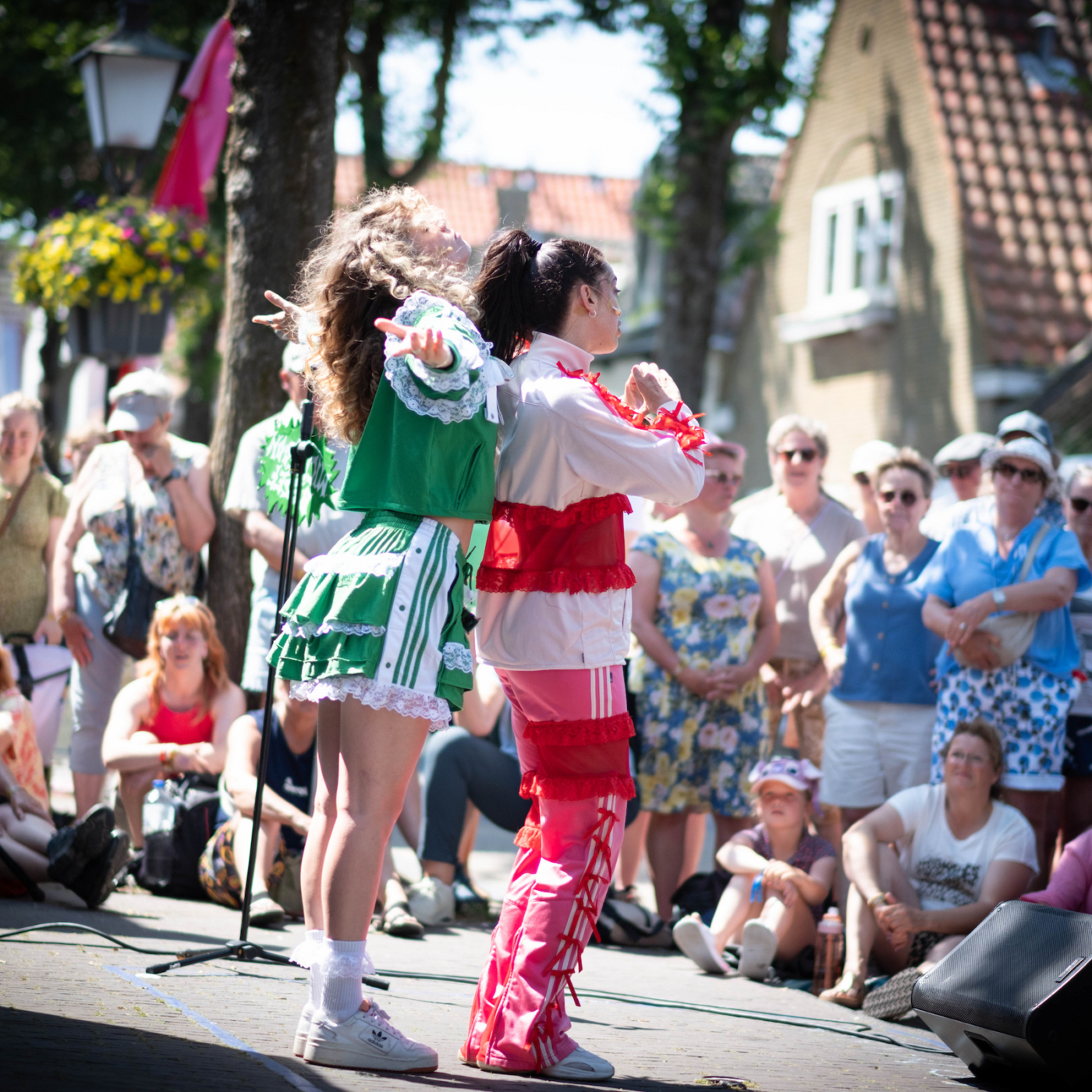 Twee dansers in kleurrijke kostuums treden op tijdens een zonnig straatfestival voor een grote toeschouwende menigte.