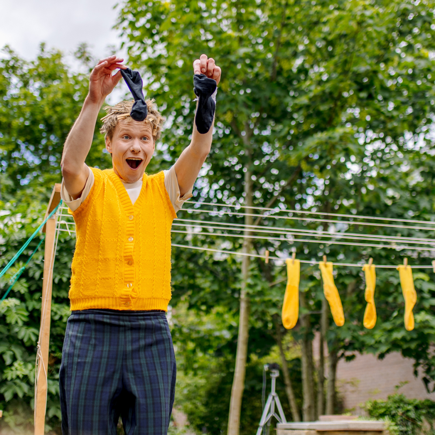 Enthousiaste man in geel vest houdt twee zwarte sokken omhoog, op de achtergrond hangen gele sokken aan een droogrek buiten.